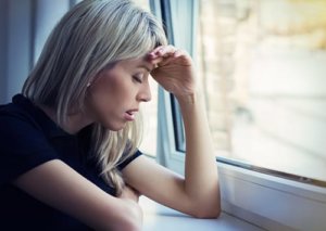 A woman leans against a windowsill as she wonders if she needs an alcohol withdrawal treatment center