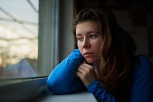 A woman stares out the window thinking about her addictive behaviors