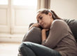 A woman sitting on the couch with her head resting on her arm.