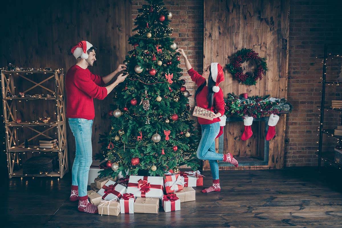 Two people decorating a christmas tree with presents.
