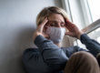 A woman with her hands on her head wearing a mask.