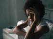 A woman sitting on the bed with her head in her hands.