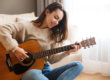 A woman sitting on the floor playing an acoustic guitar.